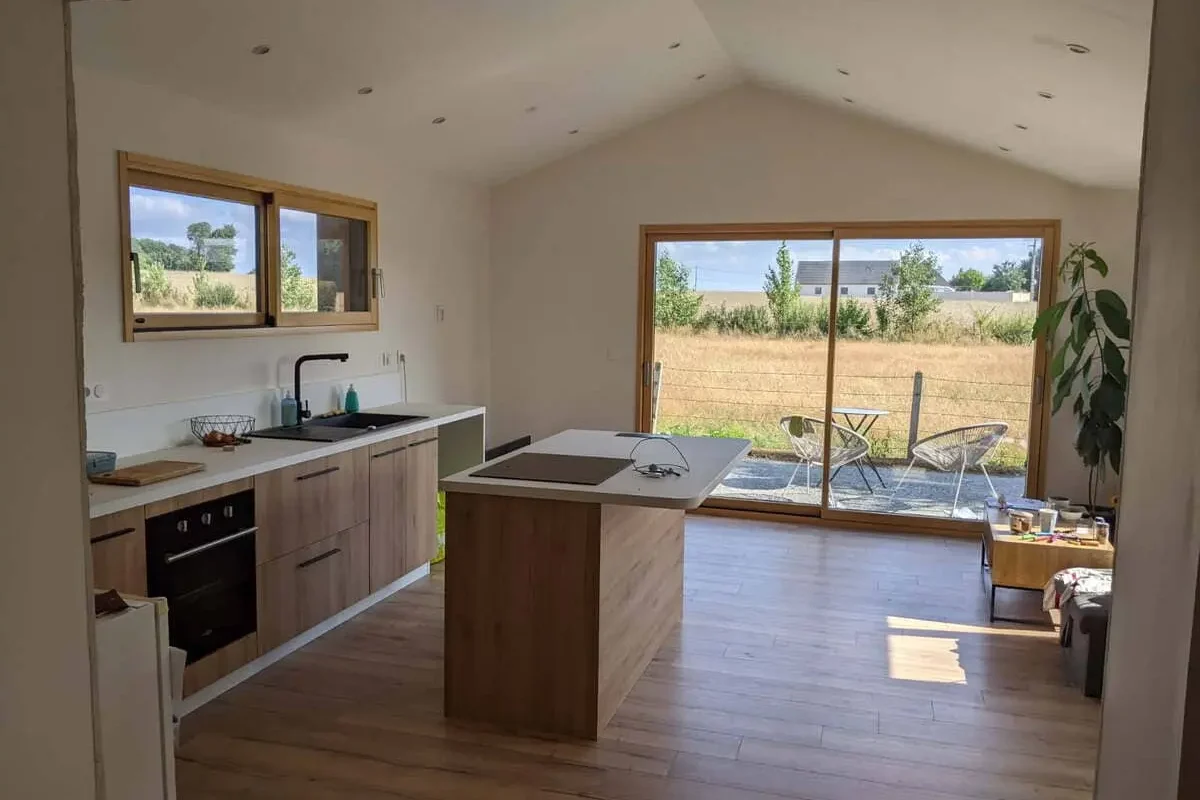 Cuisine ouverte avec îlot, armoires en bois et grandes portes coulissantes donnant sur la campagne